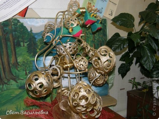 Фон, конечно, не самый подходящий, но на момент съёмки не ставилась задача размещать фото на сайте... Так, для себя, на память снимала. Поэтому не обессудьте. А на заднем плане - просто фрагмент ещё одной работы, будет случай - покажу и её... Моя подруга Наташа придумала название этой работы: " С подарками - в Россию!" Дракон трёхглавый несёт кучу шаров - подарков! Но сам он, к сожалению, слился с фоном... Все три головы украшены коронами из уже знакомых моим гостям материалов - кожуры апельсинов, украшенной блестками и стразами. Дракона связала крючком одна из учениц подруги. Он такой милашка! Хвост и гребень на его спине украшены "пружинками" из кожуры. Сам он сидит в некоем подобии корзины на проволочной конструкции, к которой подвешены собственно подарки... (фото 2)