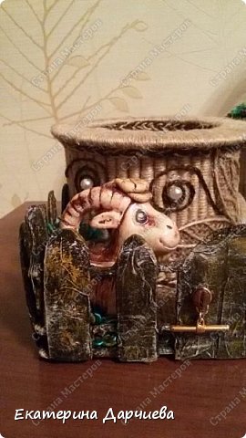 Садовый участок был готов,вернее болтался без дела больше месяца(хотела сделать на нем избушку на курьих ножках,но хотение ушло))) и вот настал его звездный час!))делала я его из картона,а потом для экономии краски обклеила зелеными салфетками(планировался зеленый)подкрасила малек забор в более
коричневый. Покрыла лаком и прикрепила ручку к калитке-застежка от бус,очень удачно вписалась! На дно участка наклеяла мешковину,для идеологической связи со шпагатными стаканами и угол между полом и забором для красоты проклеяла зеленой косичкой из пряжи. Из этой же зеленой пряжи сделала траву в горшке для дерева и на внутренних углах участка(жаль не видно)козел тоже в траве))) (фото 2)
