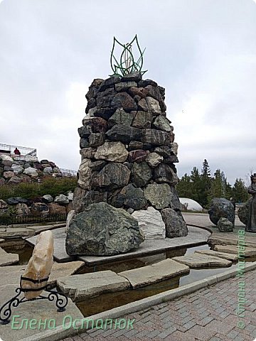 Поднявшись наверх на смотровую площадку, Вам откроется вид на нижнюю часть парка с одной стороны и на город Златоуст и горы вокруг- с другой. На переднем плане мы видим 9-метровую башню из камней с изображением Каменного цветка наверху, по ней струится вода. (фото 43)